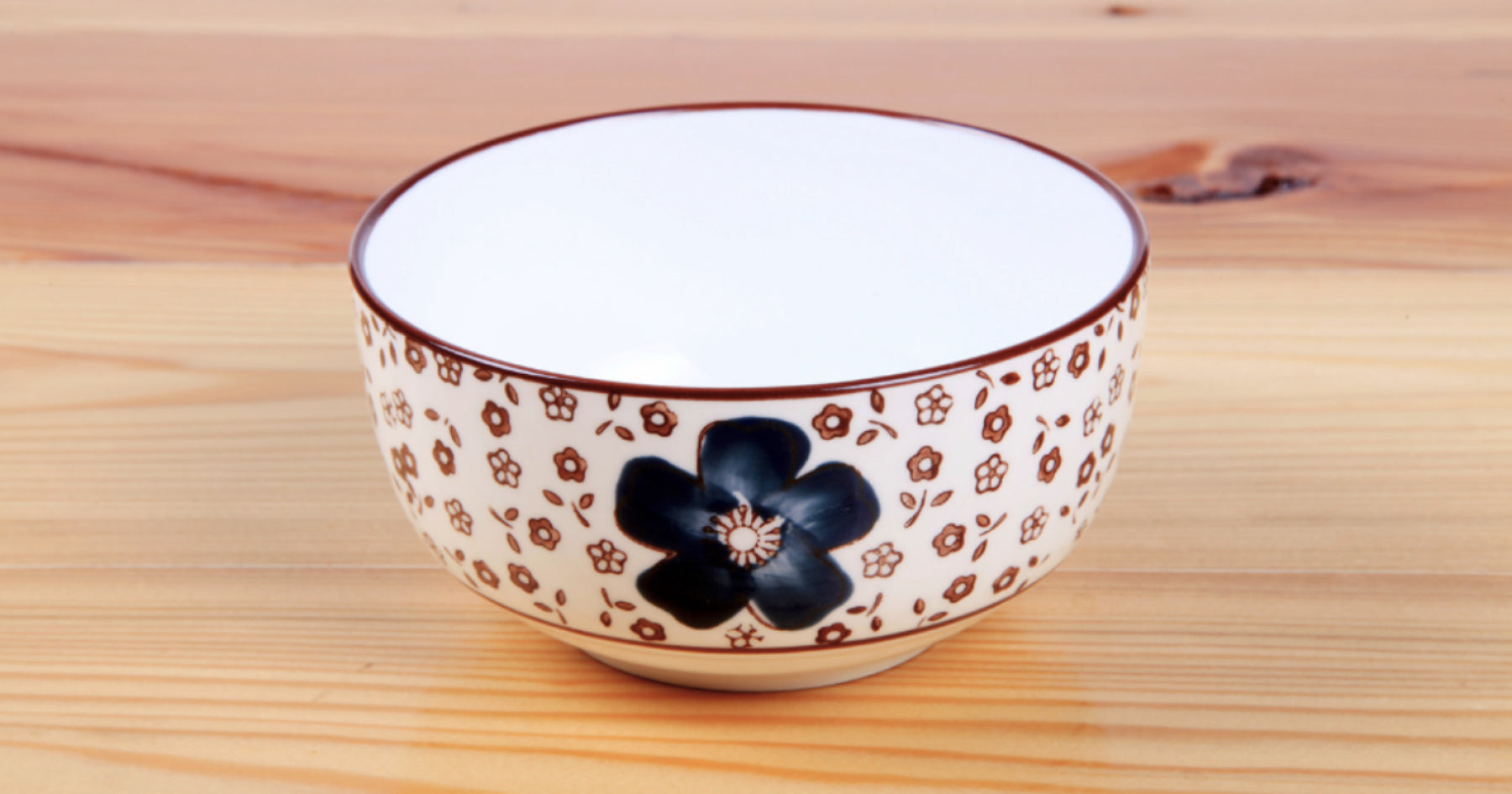 木製のテーブルに置かれた白地に茶色と黒の花柄が描かれた陶器のお茶碗。