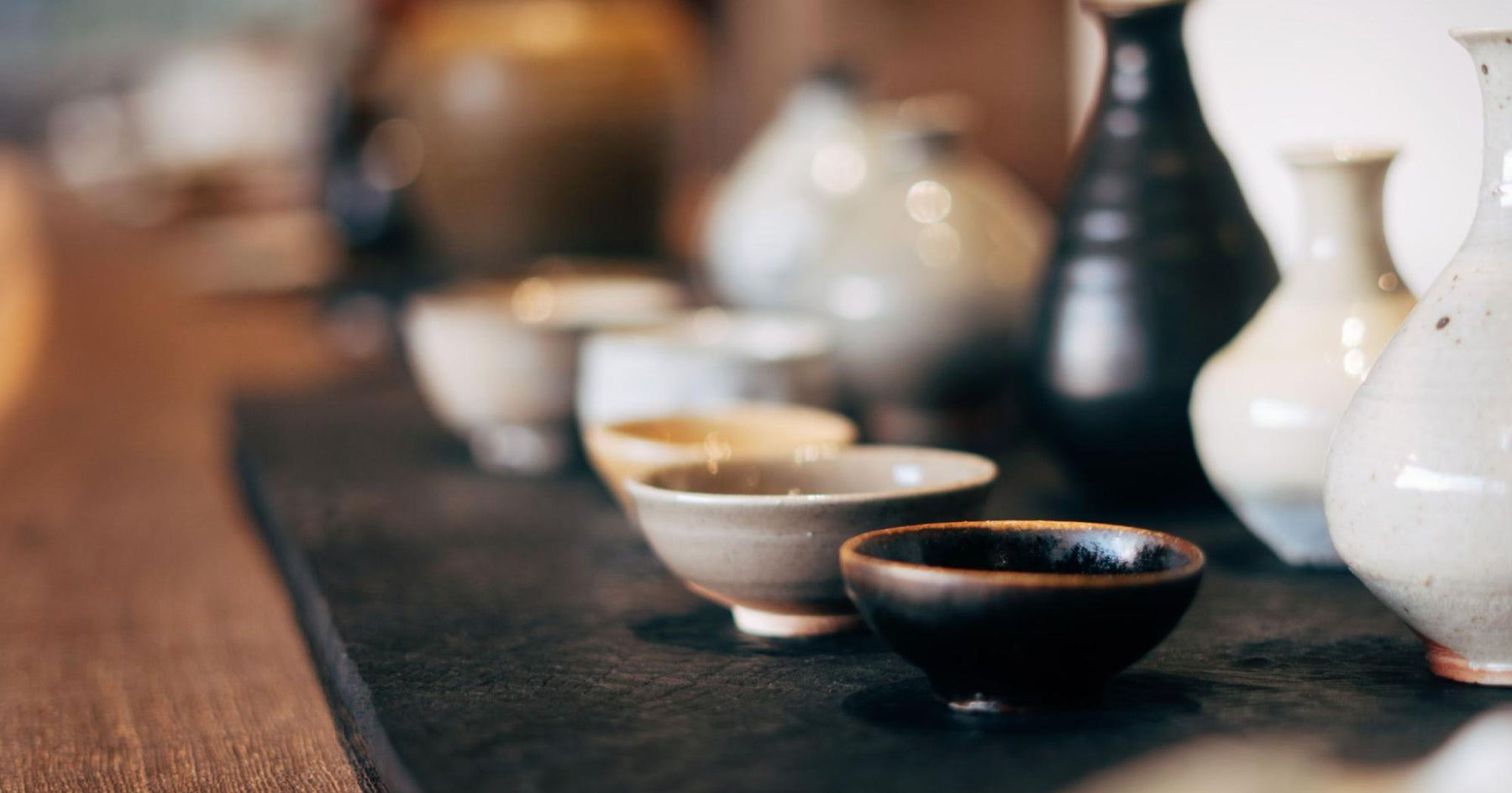 黒や白などの落ち着いた色味の酒器が黒いトレーの上に並べられている。それらが置いてあるテーブルは深い茶色の木製である。