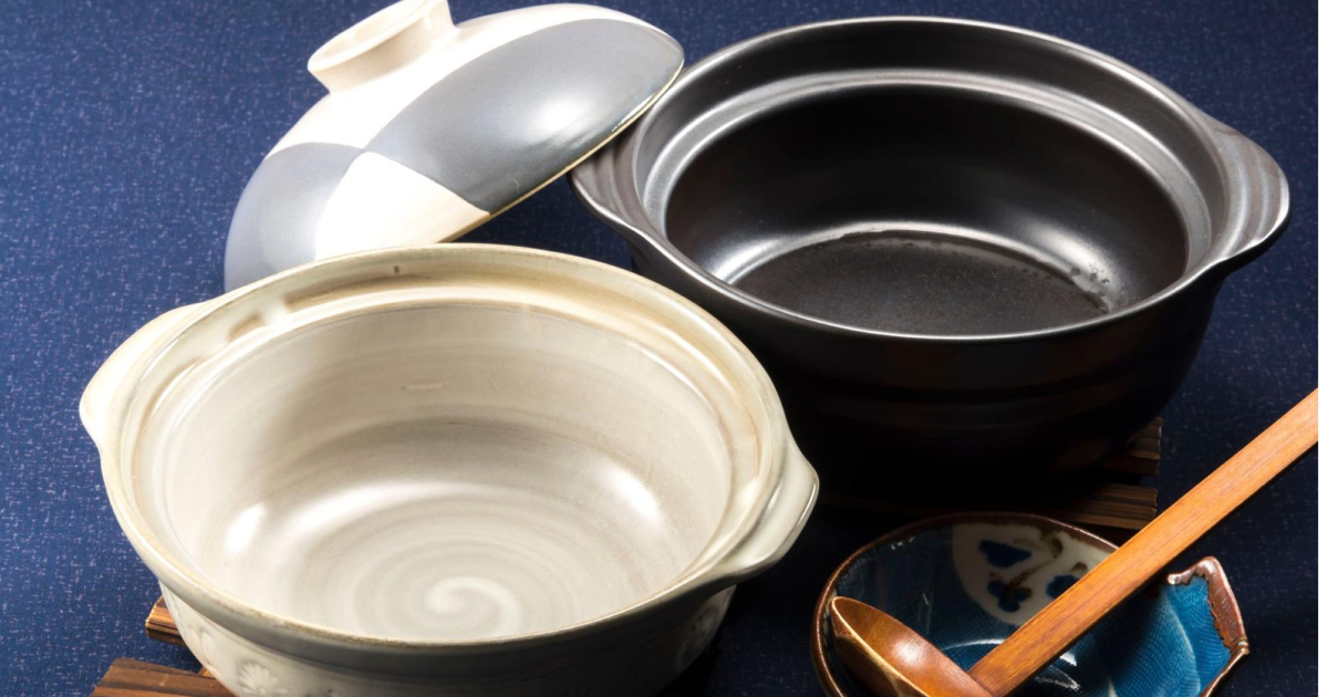 二つの土鍋と木製のスプーン、そして小皿が並んでいる。蓋を外した土鍋の内側が見えており、一つは白い色調、もう一つは黒い色調。背景は青色の布。