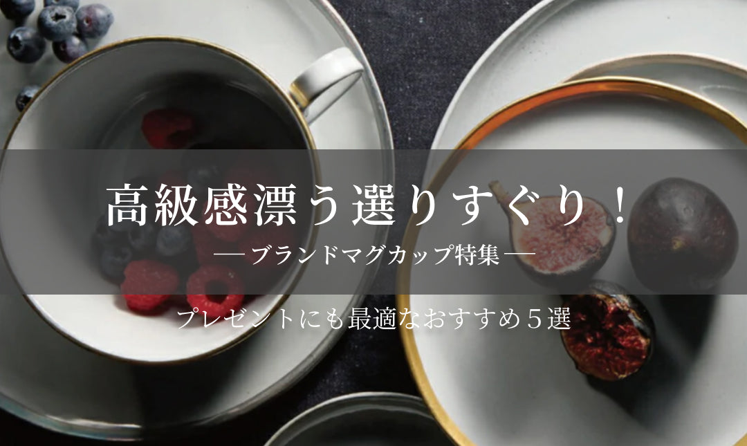黒いカップに赤いラズベリーとブルーベリーが入った食卓の風景。周りにはイチジクや金縁の皿が並んでいる。高級感のあるマグカップ特集のバナー。