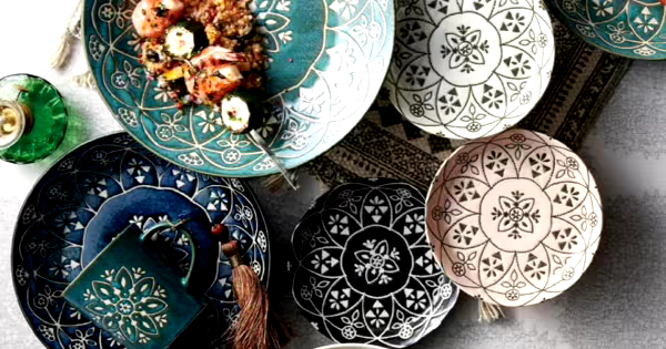 複数のカラフルな模様入りの食器が並べられたテーブル。青や白、ピンクなどの色の皿やカップがあり、ひとつの皿には料理が盛り付けられている。