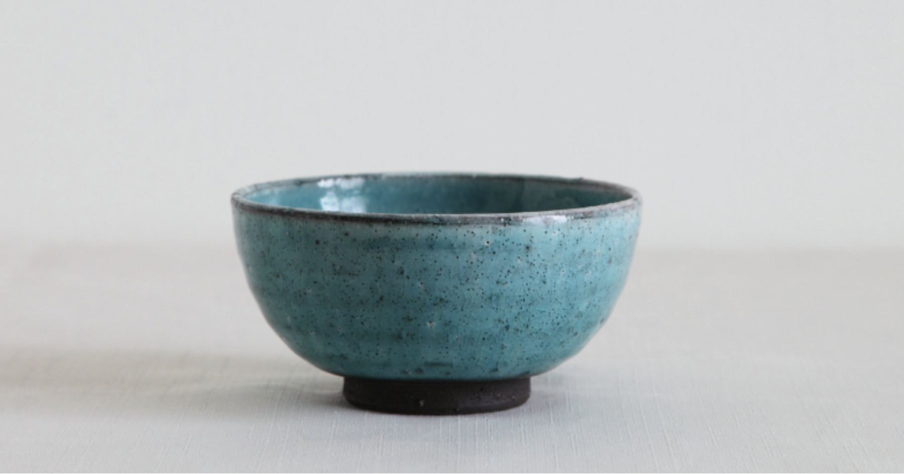 青い陶器のお茶碗。白い背景に置かれているシンプルなデザイン。