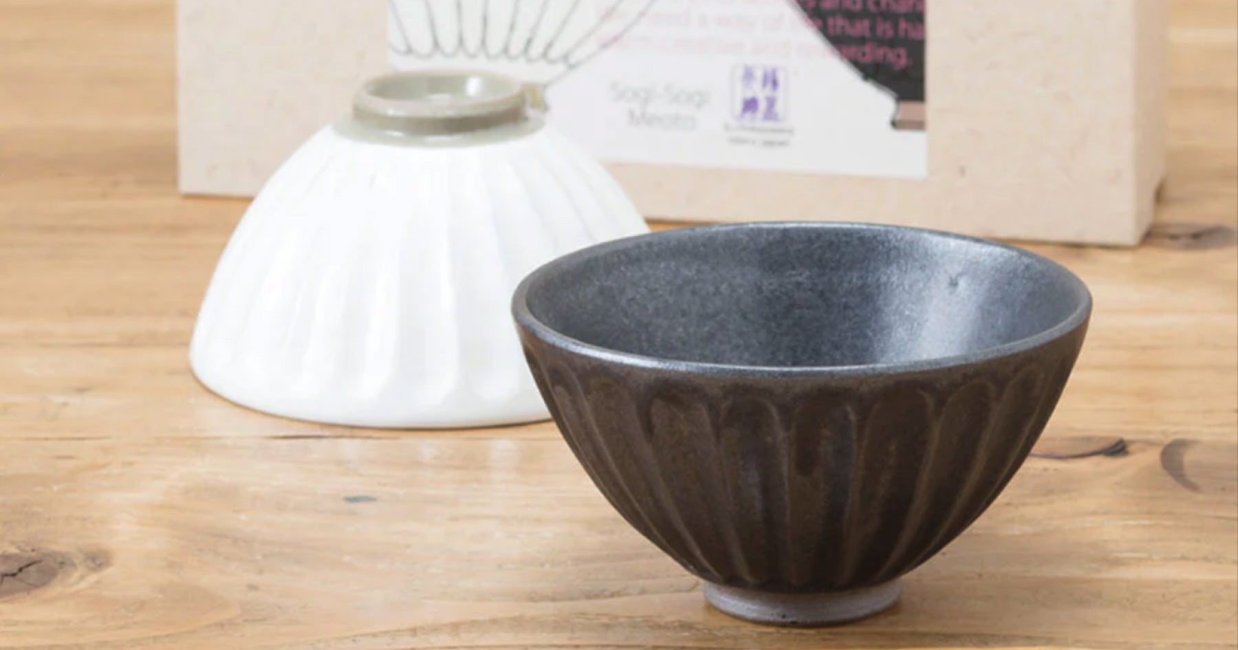 木製のテーブルに置かれた黒い陶器のお茶碗と、背景にある逆さまの白いお茶碗。