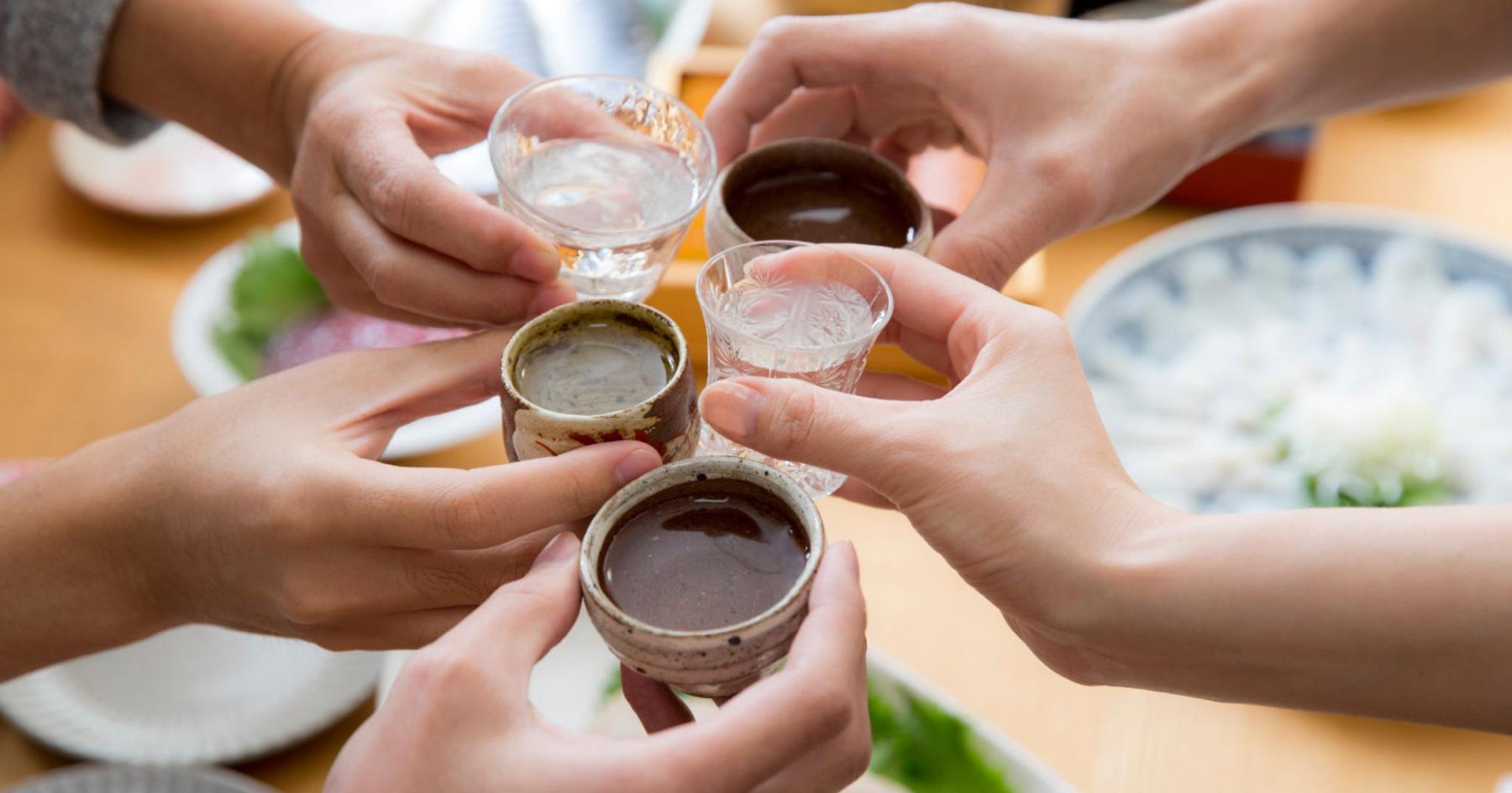 多様な酒器を5人がそれぞれ手に持ち、乾杯をしている様子。刺身などがテーブルに並んでいる。