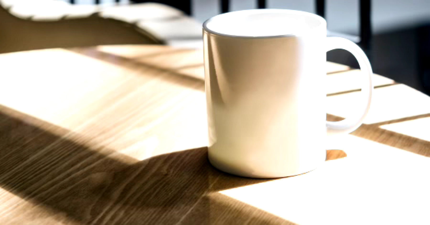 日光が差し込む木製のテーブルの上に置かれた白いマグカップ。シンプルで落ち着いた雰囲気。