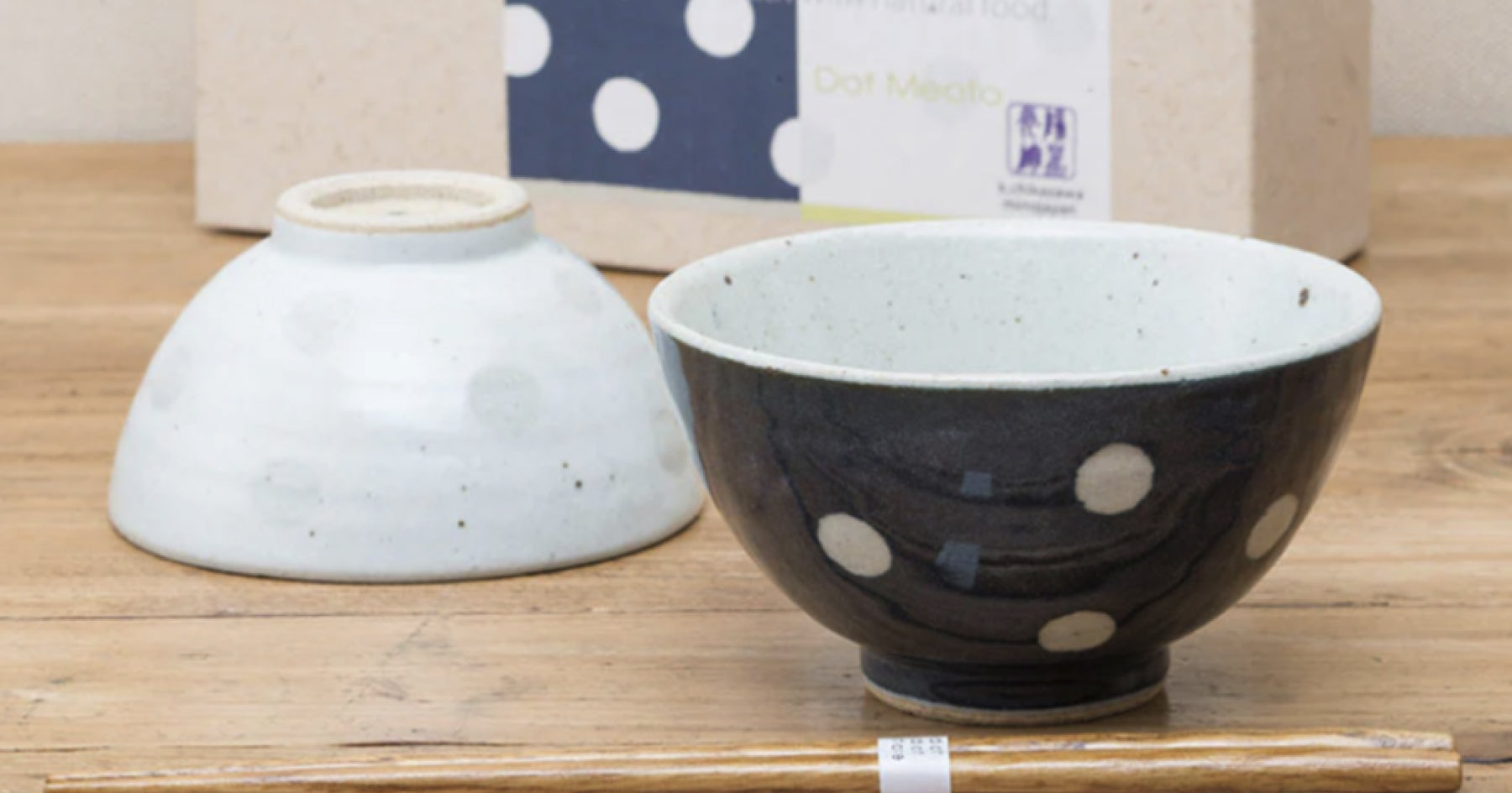 木製のテーブルに置かれた黒地に白い水玉模様の陶器のお茶碗と、背景にある逆さまの白地に白い水玉模様の陶器のお茶碗。